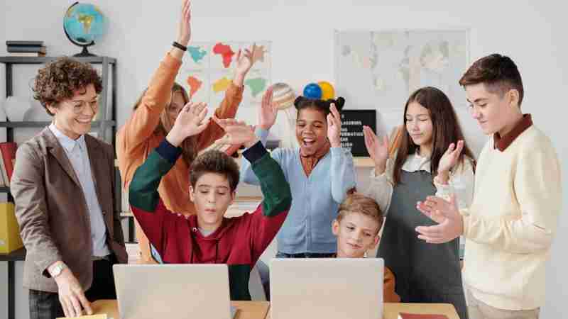 A group of happy students and a teacher clapping together in a school classroom., tags: und - pexel